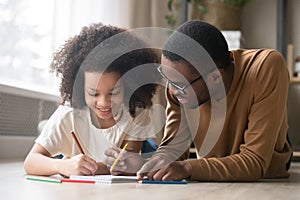 Caring black dad drawing with colored pencils teaching child girl