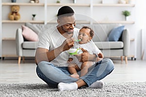 Caring Black Dad Feeding His Adorable Infant Baby From Spoon At Home