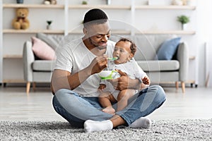 Caring Black Dad Feeding His Adorable Infant Baby From Spoon At Home photo