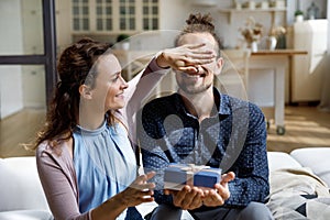 Caring cheerful young woman giving gift box to joyful husband.