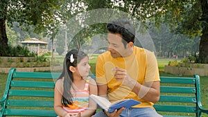 Caring dad reading out an interesting story to his little child sitting outdoors
