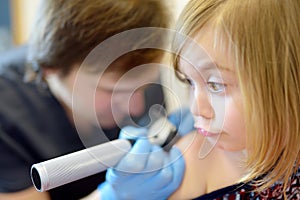 A caring doctor checks moles on the skin of a small child. A dermatologist looks at a rash on the back of a girl using a