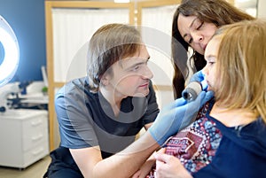 A caring doctor checks moles on the skin of a small child. A dermatologist looks at a rash on the neck of a girl using a