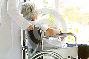 Caring doctor or nurse supporting disabled,alzheimer senior asian woman on wheelchair,female caregiver walking,elderly patient photo