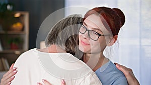 Caring for elderly, female social worker in medical uniform helps and supports an old woman, hugs and rubs her hand on