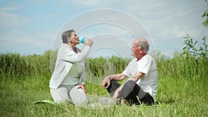 Caring elderly man gives cool clean water in sports nutrition bottles to his dear beloved wife after playing sports or