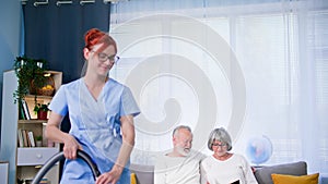 caring for elderly, young female social worker in a medical uniform helps an elderly man and woman with cleaning the
