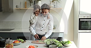 Caring father cook salad at kitchen piggybacking cute little daughter