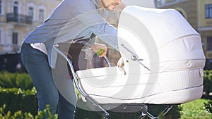 Caring father feeding baby in stroller, conscious parenthood, walk in park