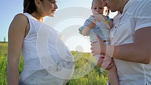 Caring father holding toddler daughter and touching pregnant mother belly