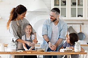 Caring father and mother playfully teaching little children to cooking.