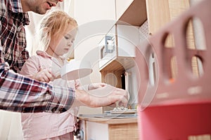 Caring father plays with his cute daughter in a small children kitchen, in a cozy home. Lifestyle.