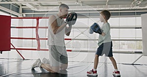 Caring father professional boxer teaching son martial arts sparring with kid explaining moves in gym