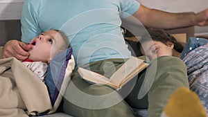 Caring father reading bedtime story to his children at home. Evening family reading. Kids listening dad, reading a