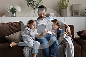 Caring father reading book to little daughter and son