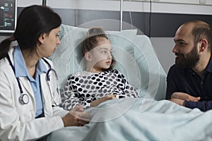 Caring father sitting next to sick daughter resting in hospital pediatric ward