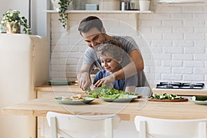 Caring father teach little son chopping vegetables