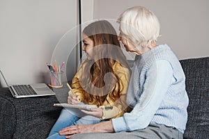 Caring grandmother keeping eye on child having remote lesson