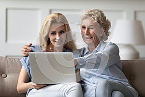 Caring grown up daughter teaching elderly mother to use laptop