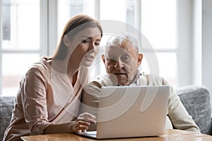 Caring grownup daughter teaching elderly father to use laptop