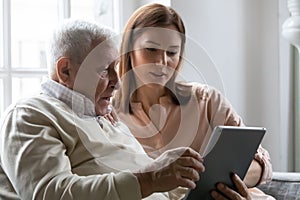 Caring grownup daughter teaching elderly father to use tablet photo