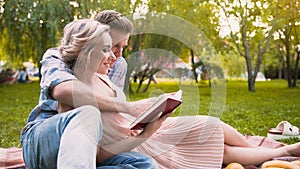 Caring guy reading story to his beautiful lady, gently hugging her, date in park