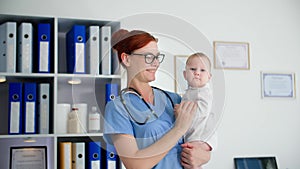 caring for health of babies, portrait of a young female doctor in glasses with a small child in her arms standing in a