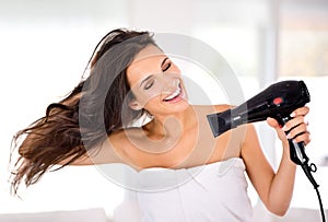 Caring for her hair. A beautiful woman smiling while drying her hair with a hairdryer.