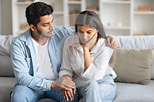 Caring indian husband soothing his distressed wife on sofa