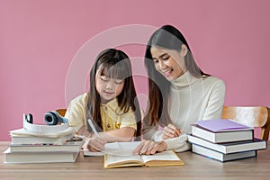 A caring and kind Asian private teacher is teaching and helping a young little girl do homework