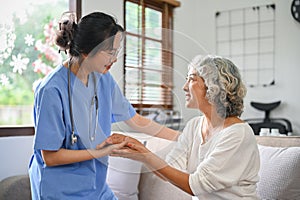 Caring and kind young Asian female doctor or nurse holding an aged female`s hands to comfort