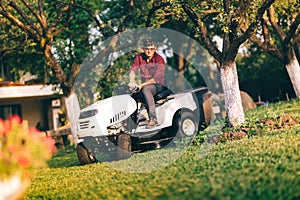 Caring lawncare concept - handsome young man trimming grass in garden using tractor