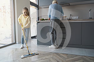 Caring little girl cleaning the floor while assisting her grandma