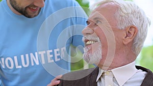 Caring male volunteer talking to aged lonely man during walk in park, assistance