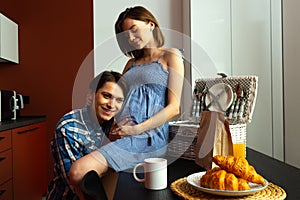 Caring man hugging pregnant woman belly in kitchen