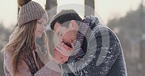 A caring man warms his wife`s hands in the winter on the street in a snow-covered Park.