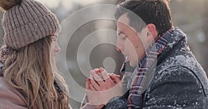 A caring man warms his wife`s hands in the winter on the street in a snow-covered Park.