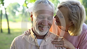 Caring mature wife flirting with handsome husband in park, whispering compliment