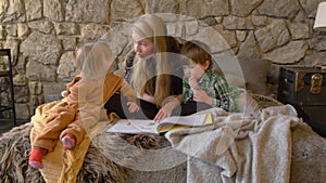 Caring mom babysitter, parent mother reading for son and daughter a book in bed before going to sleep