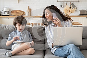 Caring mom business lady talk to small son during phone call working on laptop computer at home