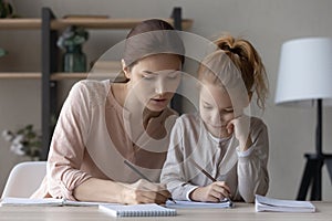 Caring mom and little daughter study together at home