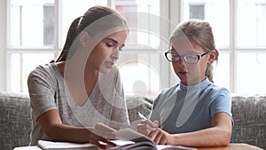 Caring mom teacher helping kid daughter with homework at home