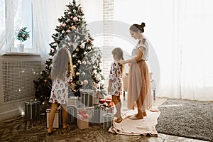 Caring mother braids her little daughter`s braid while second daughter decorates a New Year`s tree in the light cozy