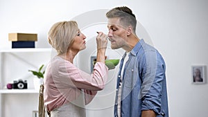 Caring mother feeding adult son with spoon, negative side of overprotection