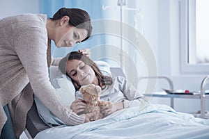 Caring mother giving a plush toy to sick daughter lying in a hos