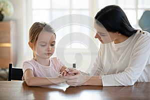 Caring mother holding upset offended little daughter hands close up