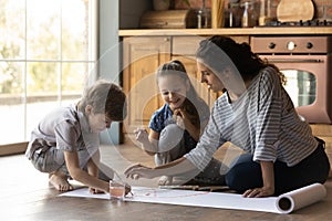 Caring mother and little kids painting watercolors at home together