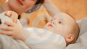 Caring Mother Lying on a Bed, Playing with a Cute Newborn Baby at Home. Mom Bonding with a Toddler