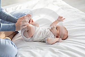 Caring Mother Making Gymnastics To Her Newborn Baby On Bed At Home