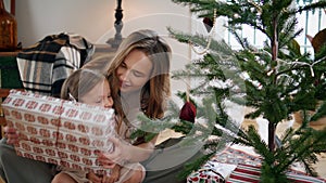 Caring mother presenting gift to baby daughter cozy place. Girl looking present